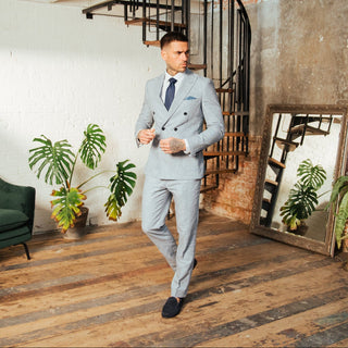 Man in a blue suit walking through a stylish room with plants and a green armchair.